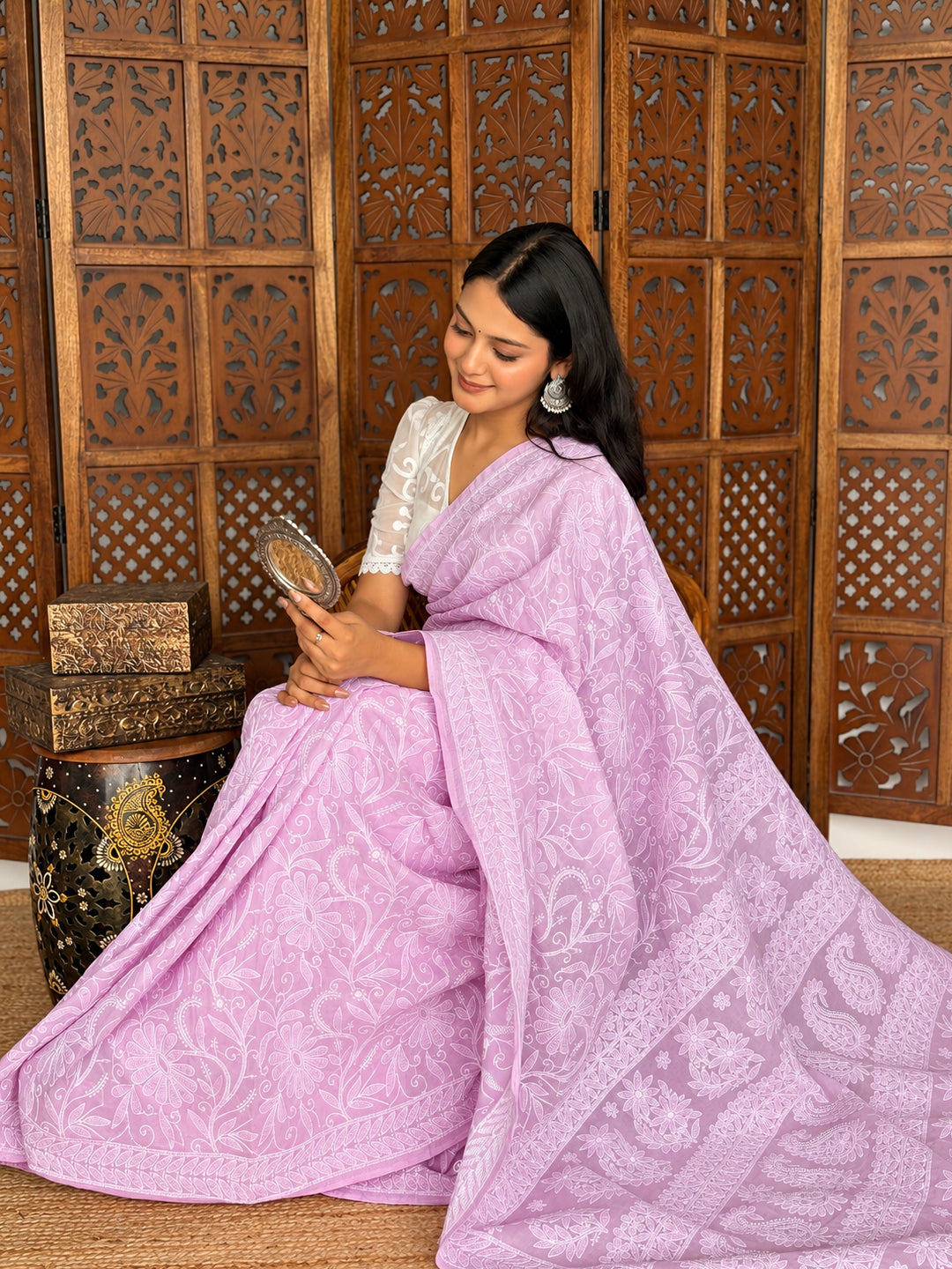 Model presenting the Adhira Cotton Chikankari Saree with one hand at her waist, highlighting the floral embroidery and neatly framed saree border.