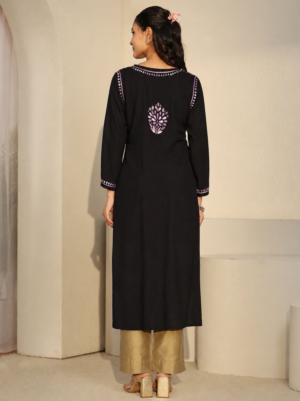 Model presenting the front design of the Ayra Chikankari kurti, with her hands resting at the waist and embroidered cuffs visible above a long front panel of scattered floral motifs.