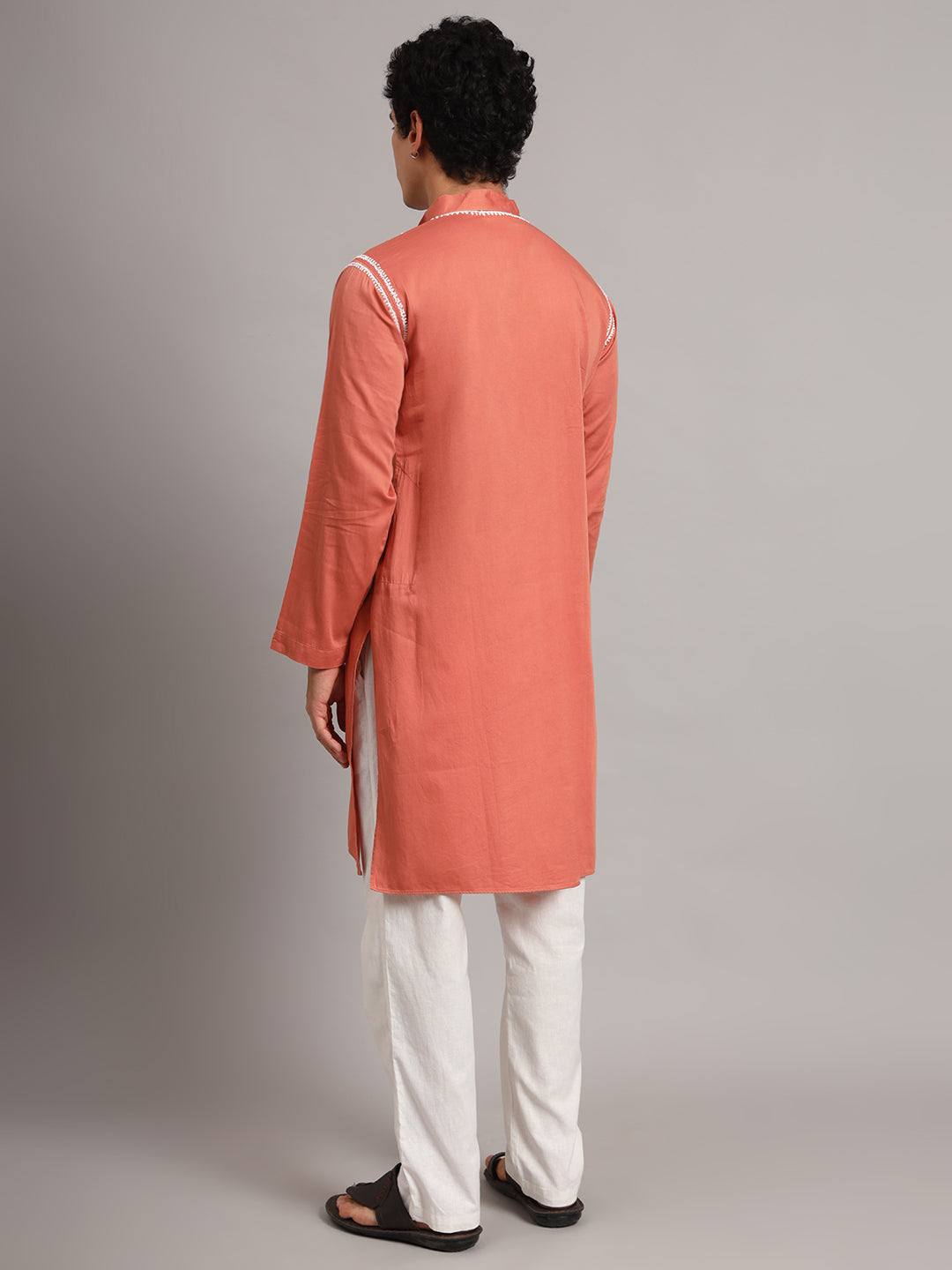Knee-length Uman Chikankari kurta for men with side openings and a buttoned mandarin collar, photographed on a model wearing straight trousers and sandals.