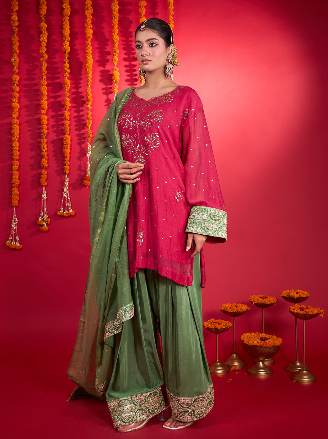 Model wearing the Noorani Mul Chanderi Short Kurti Farshi Set with floral embroidery, wide-leg pants and a coordinating dupatta against a festive backdrop.