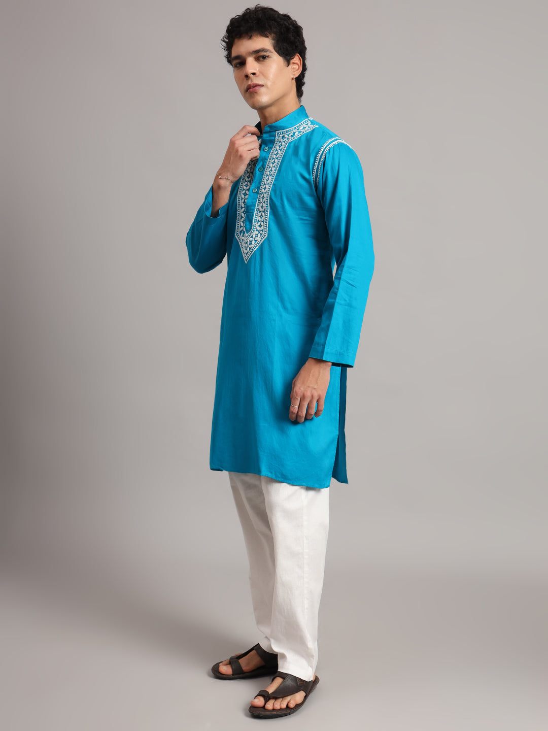 Uman Chikankari kurta for men photographed against a plain studio backdrop, showing long sleeves, a straight hem and side slits above the trouser legs.