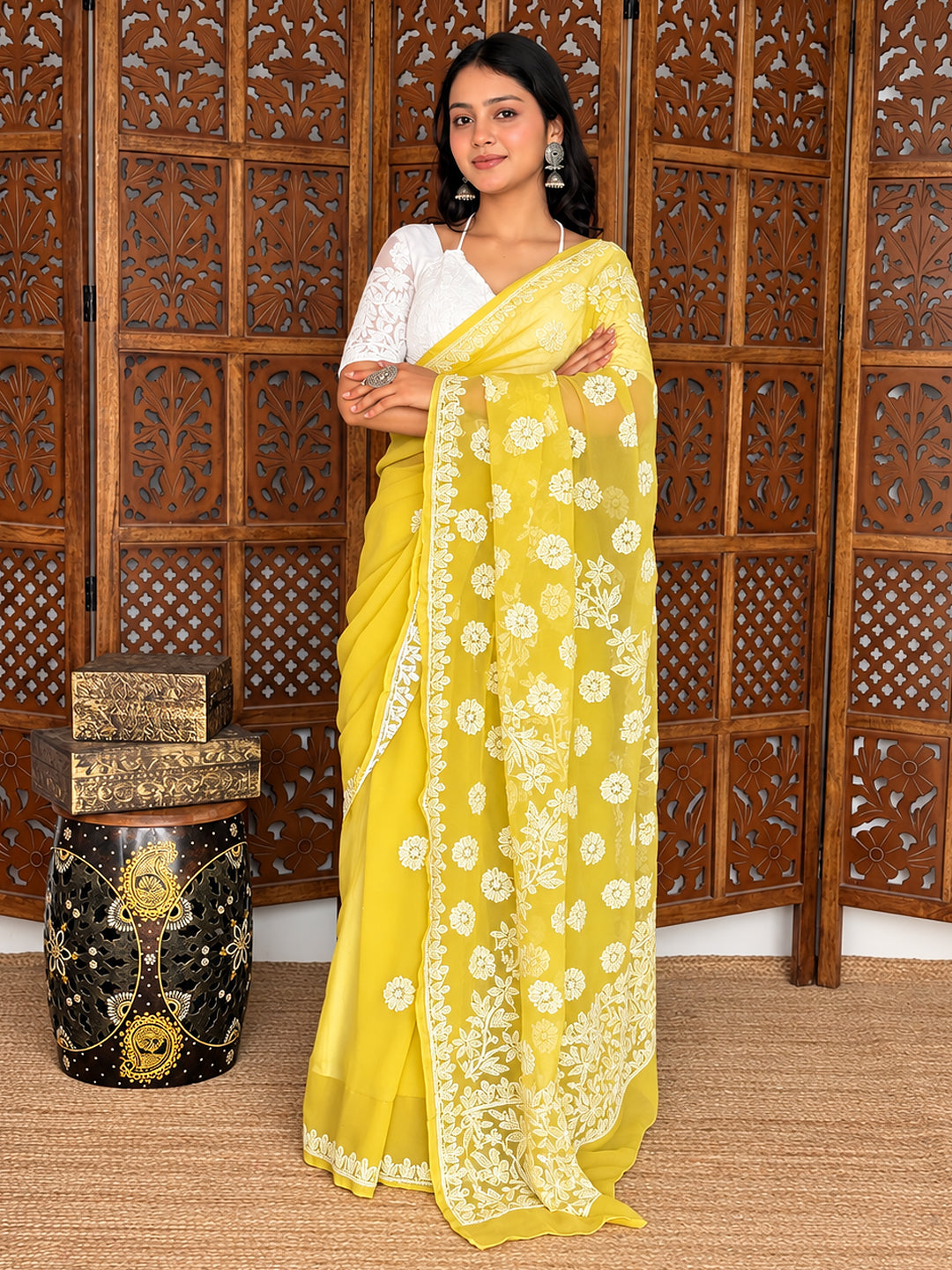 Pranshi Georgette Chikankari Saree styled with an embroidered blouse, traditional earrings and stacked bangles against a carved wooden backdrop.