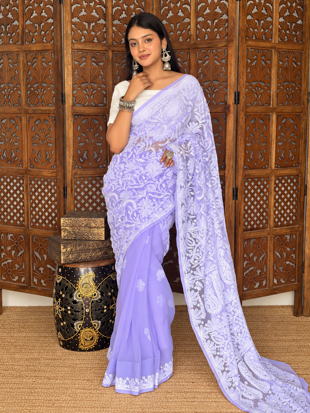 Model wearing the Sahira Georgette Half Jaal Saree with floral Chikankari embroidery, pleated draping and an extended pallu against a carved wooden backdrop.