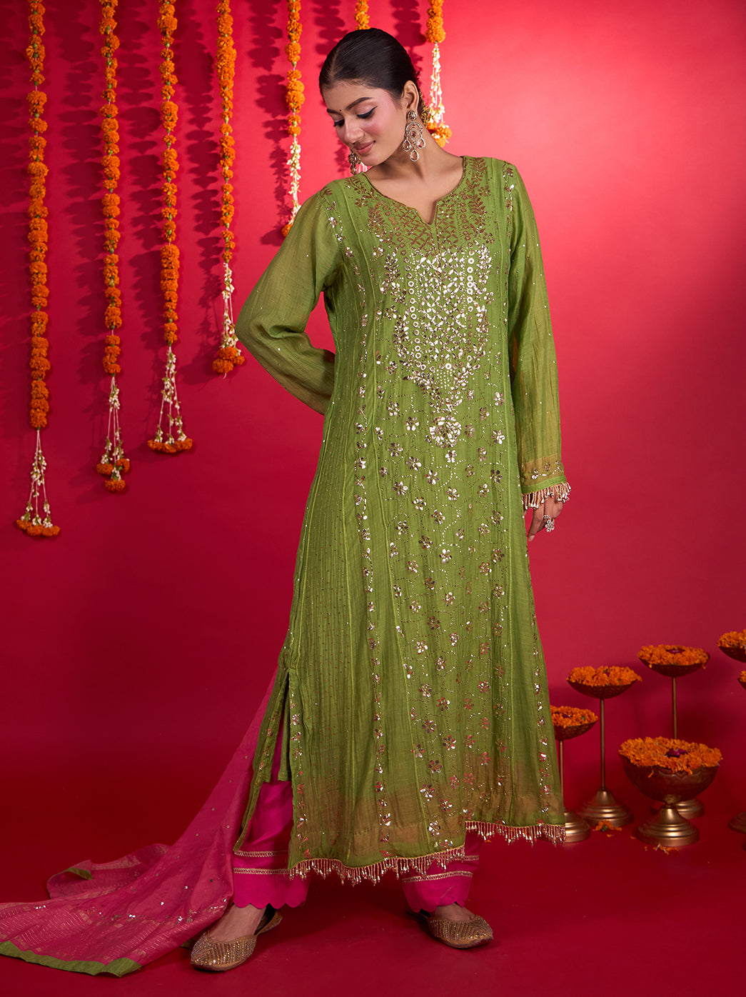 Model wearing the Tehzeeb Mul Chanderi Kurta Set with Dupatta, featuring a long embroidered kurta, coordinating bottoms and a bordered dupatta against a festive marigold backdrop.