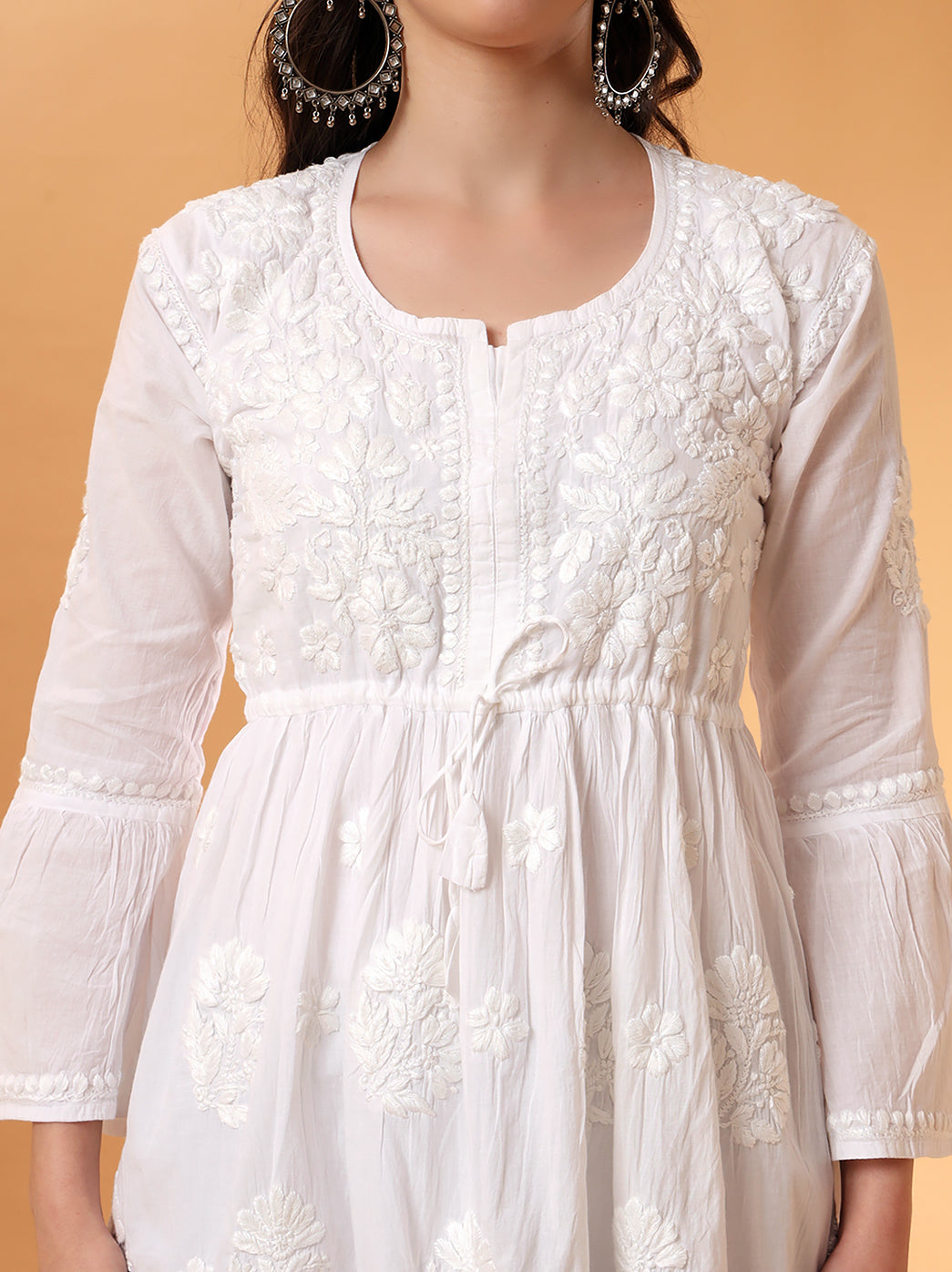 Handcrafted white chikankari short kurti with bell sleeves and peplum waist, made from soft, eco-friendly mulmul cotton.