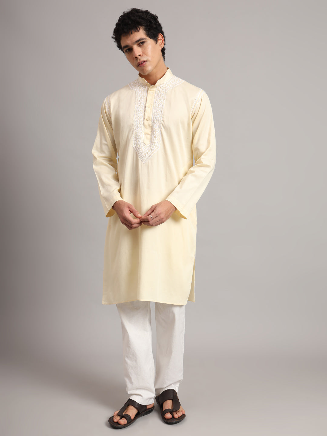 Uman Mens Kurta with full-length sleeves ending at the wrists, a buttoned neckline and a pointed embroidered chest design, paired with simple trousers and sandals.