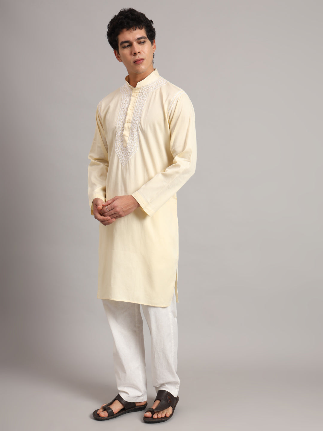 Uman Chikankari kurta styled as a complete men's ethnic outfit, with straight trousers, open-toe sandals and an embroidered neckline visible above the model's joined hands.