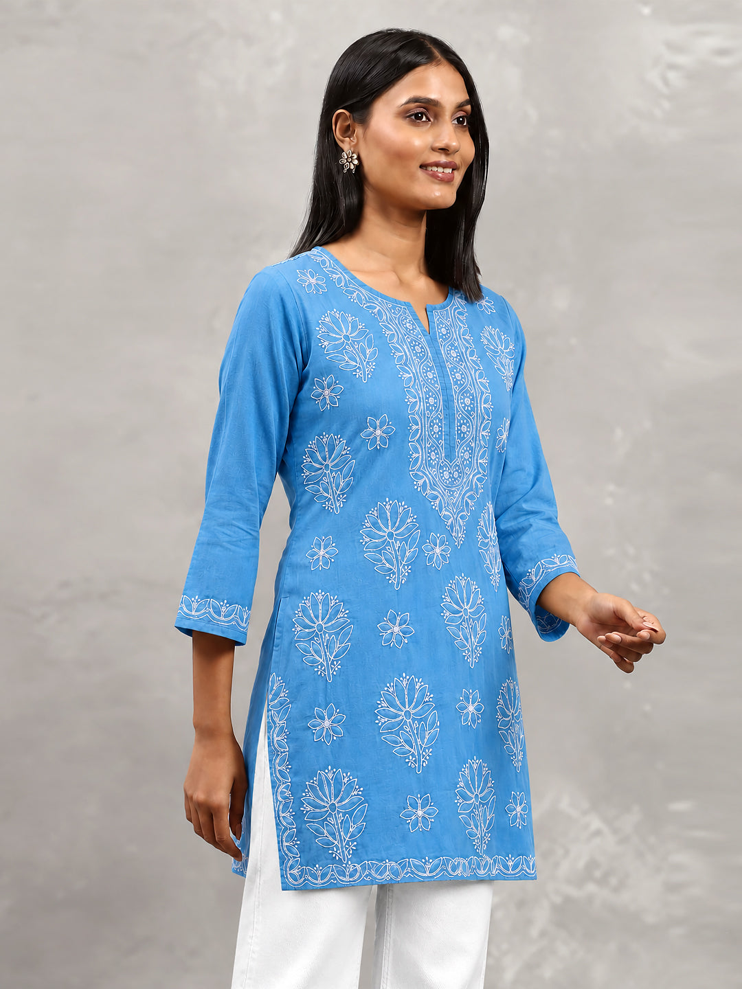 Ziva Cotton Short Kurti by The Chikan Label displayed on a wooden hanger, showcasing its straight silhouette, floral embroidery and three-quarter sleeves.