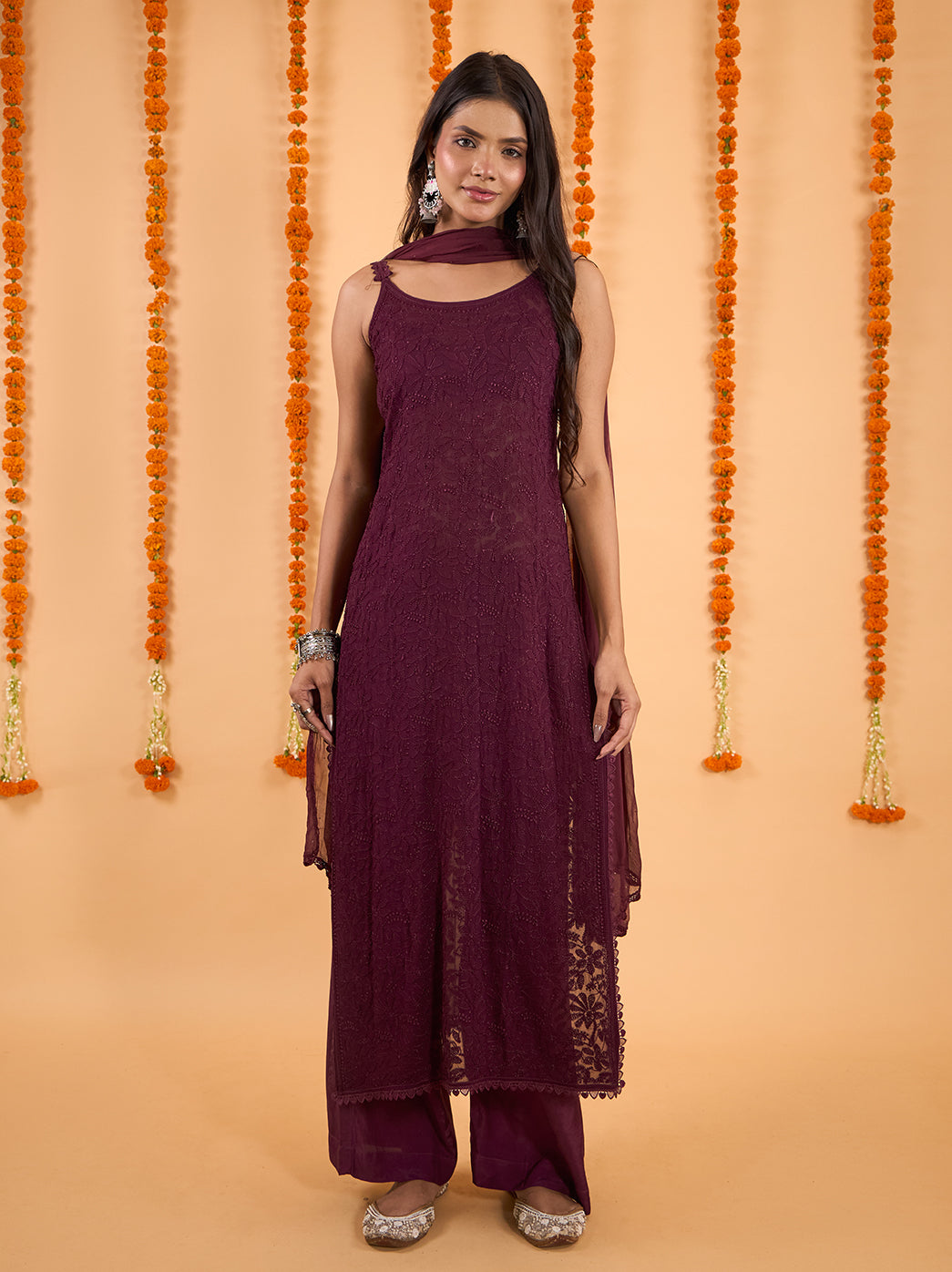 Model standing against a marigold-decorated backdrop in the Adaah sleeveless viscose kurti, palazzo pants and sheer dupatta ensemble.