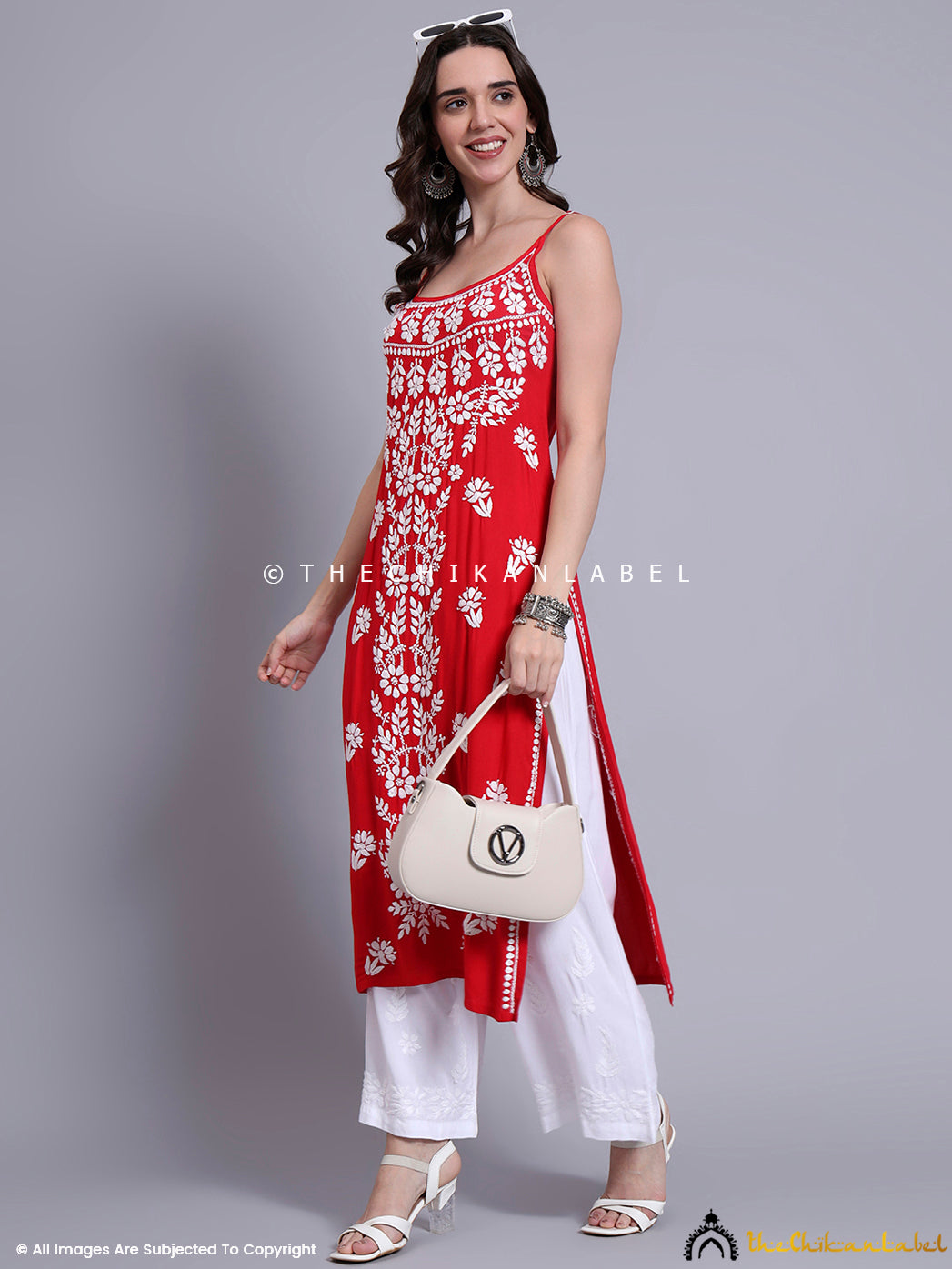 Indian woman modeling a long chikankari kurta with strappy shoulders and white embroidery motifs, styled with statement earrings and sandals.

