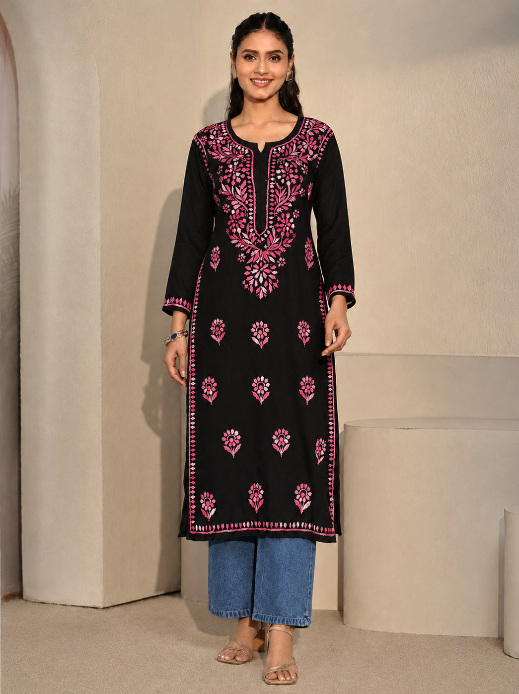 Model presenting the front design of the Ayra Chikankari kurti, with her hands resting at the waist and embroidered cuffs visible above a long front panel of scattered floral motifs.