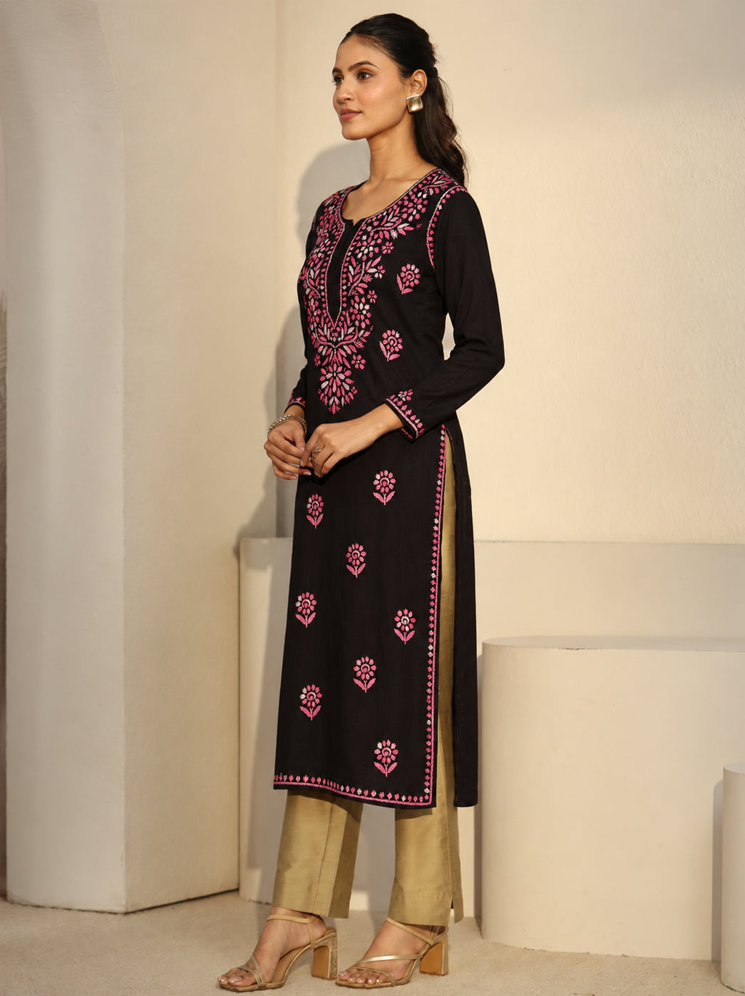 Ayra Rayon Straight Kurti photographed in a standing pose beside a curved architectural feature, with the complete embroidered front, side slits, denim trousers and strappy sandals visible.