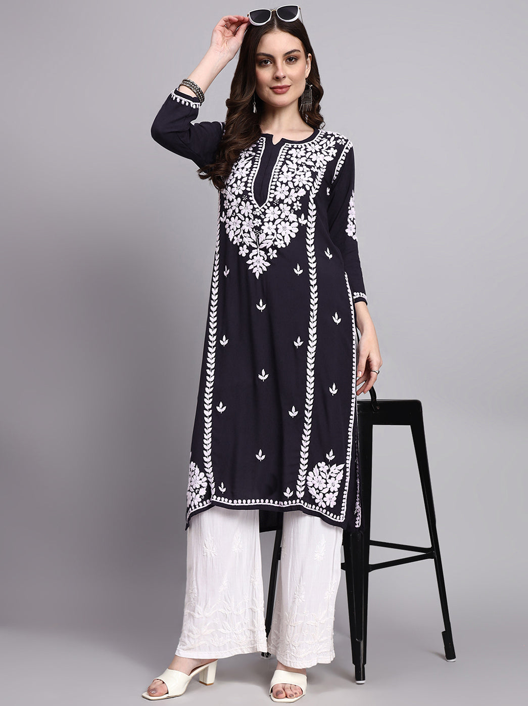 Woman wearing a black and white embroidered kurta with white pants on a gray background