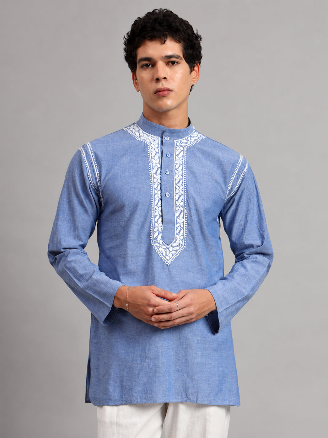 Denim Mens Kurta featuring floral Chikankari embroidery around the mandarin neckline and button placket, modelled with straight trousers and hands joined at the waist.