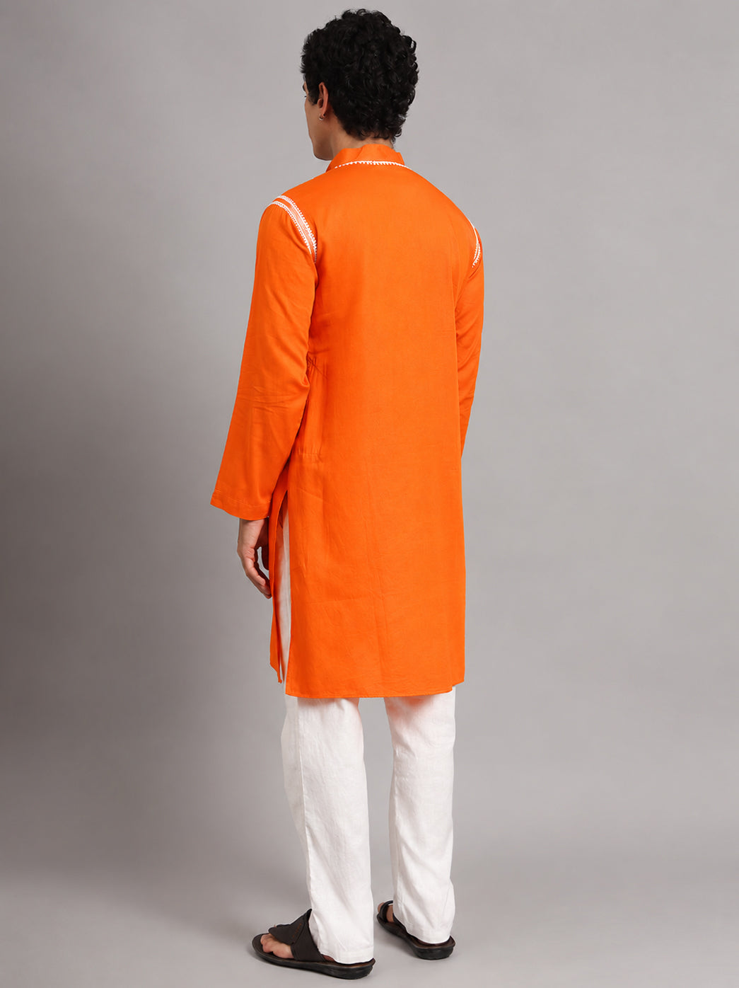 Uman Chikankari kurta styled as a complete men's ethnic outfit, with straight trousers, open-toe sandals and an embroidered neckline visible above the model's joined hands.