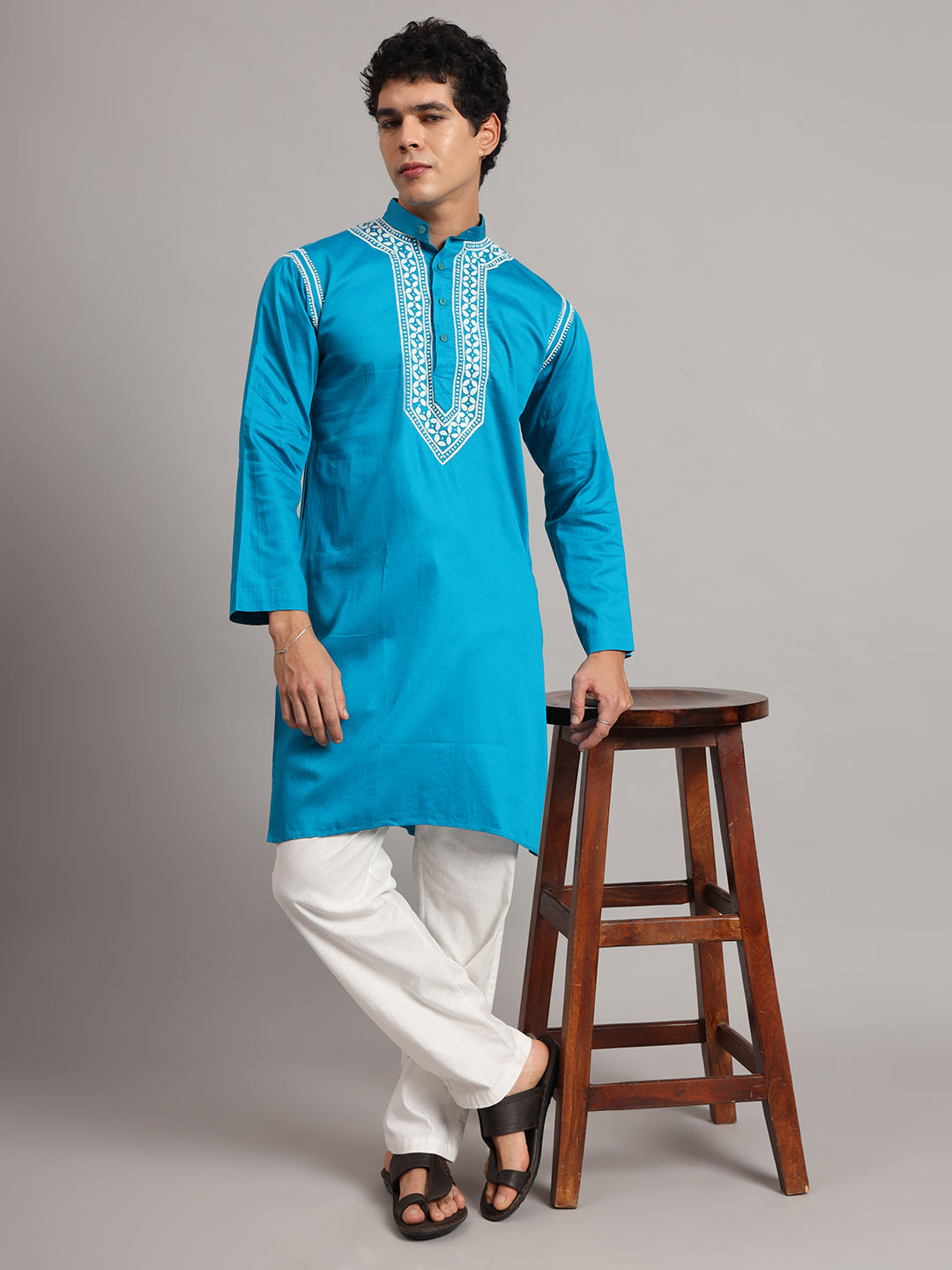 Uman Mens Kurta shown on a standing model, with floral Chikankari embroidery surrounding the button placket and extending into a pointed panel below the chest.