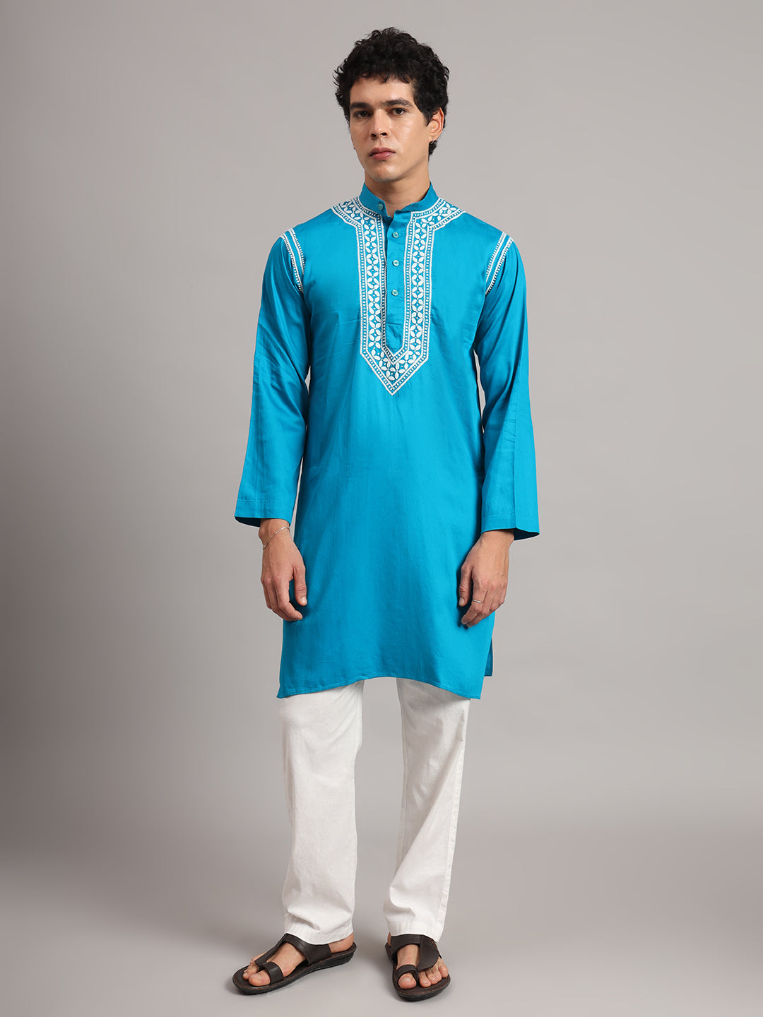 Model wearing the Uman men's kurta with hands loosely joined at the waist, displaying embroidered collar borders and leafy motifs arranged along the chest panel.