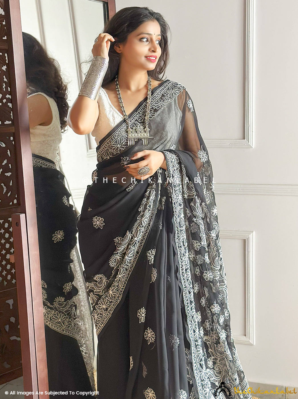 Elegant Indian woman dressed in handcrafted chikankari saree with sheer embroidered pallu and ornate borders, accessorized with statement bangles and necklace for ethnic appeal.