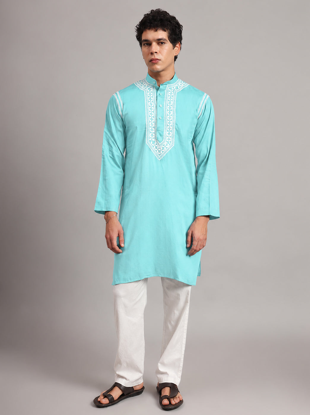 Model wearing the Uman men's kurta with hands loosely joined at the waist, displaying embroidered collar borders and leafy motifs arranged along the chest panel.