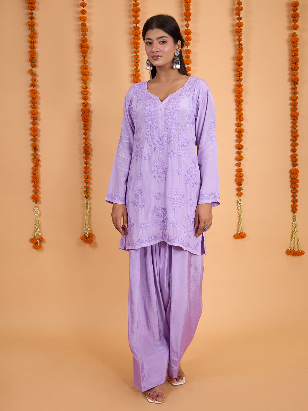 Model showcasing a muslin Chikankari short kurti with embroidered neckline and hem, paired with wide-leg Farshi pants and open-toe heels.