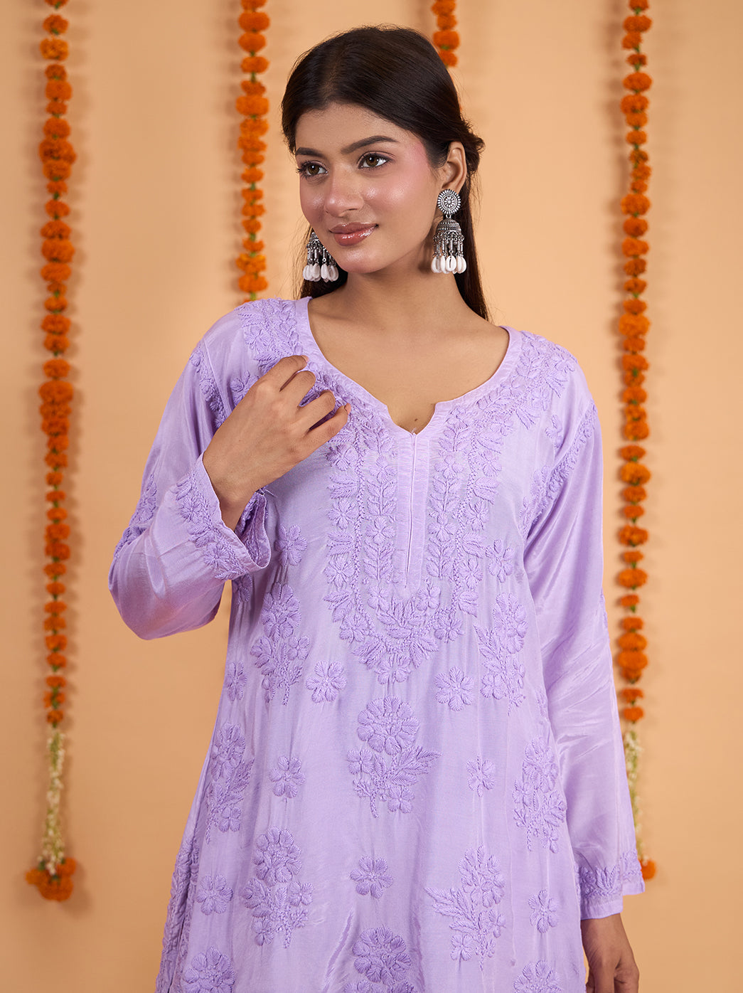 Shagun Chikankari kurta set styled for a festive occasion with silver-tone statement earrings, minimal heels and a backdrop of hanging marigold garlands.