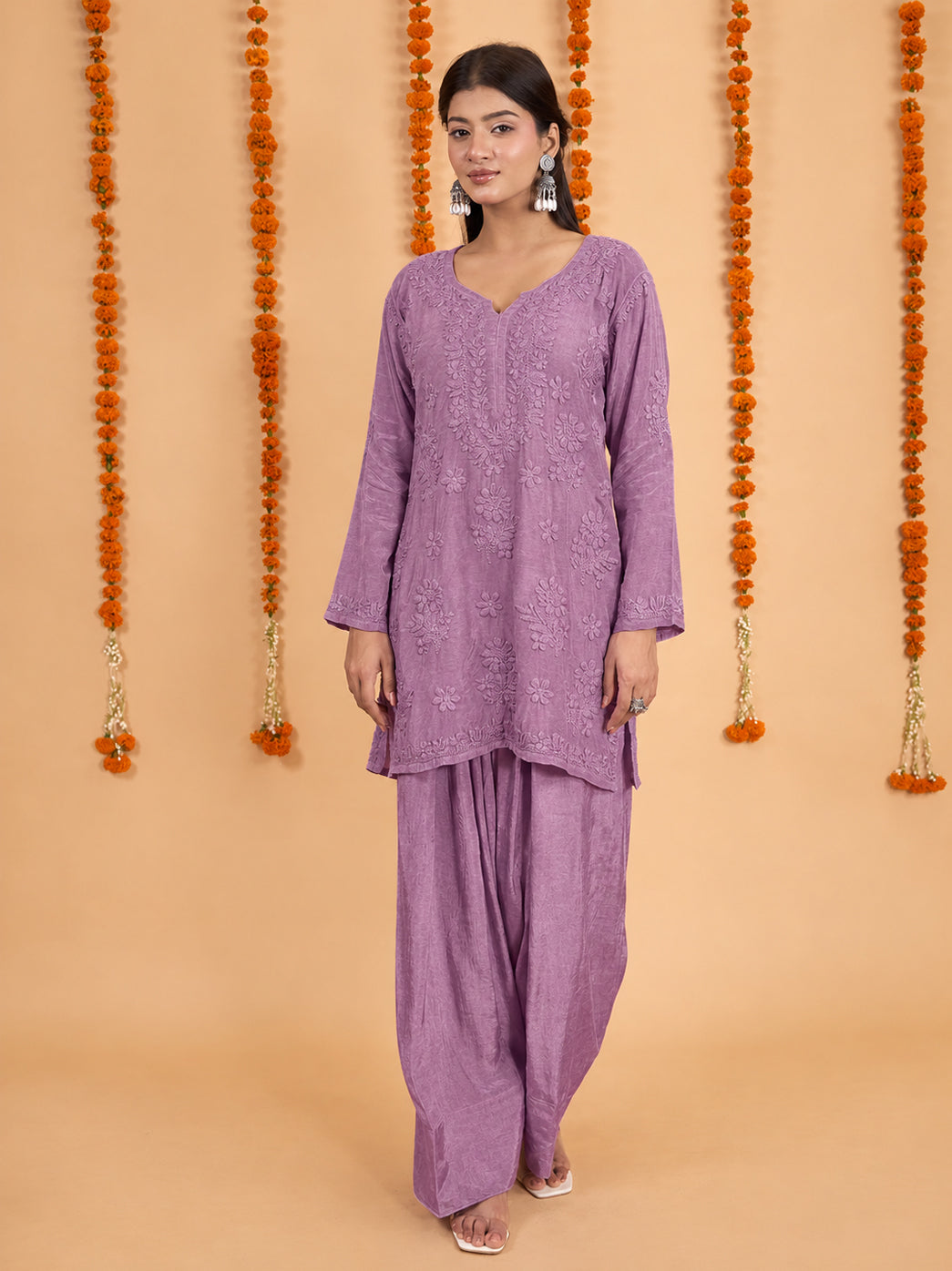 Shagun Muslin Chikankari Kurti Farshi Set photographed in a festive setting, featuring detailed floral embroidery, bordered sleeves and a short kurti over flowing pants.