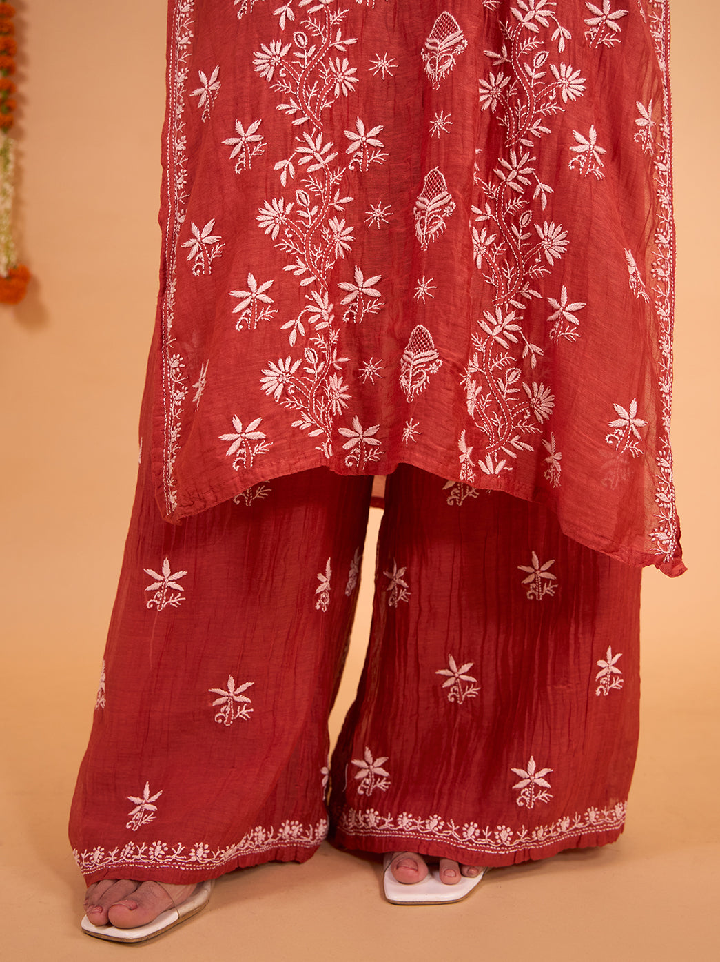 Mul Chanderi Chikankari kurta and palazzo set displayed in a festive setting with hanging marigold garlands, accessorised with jhumkas and embroidered juttis.