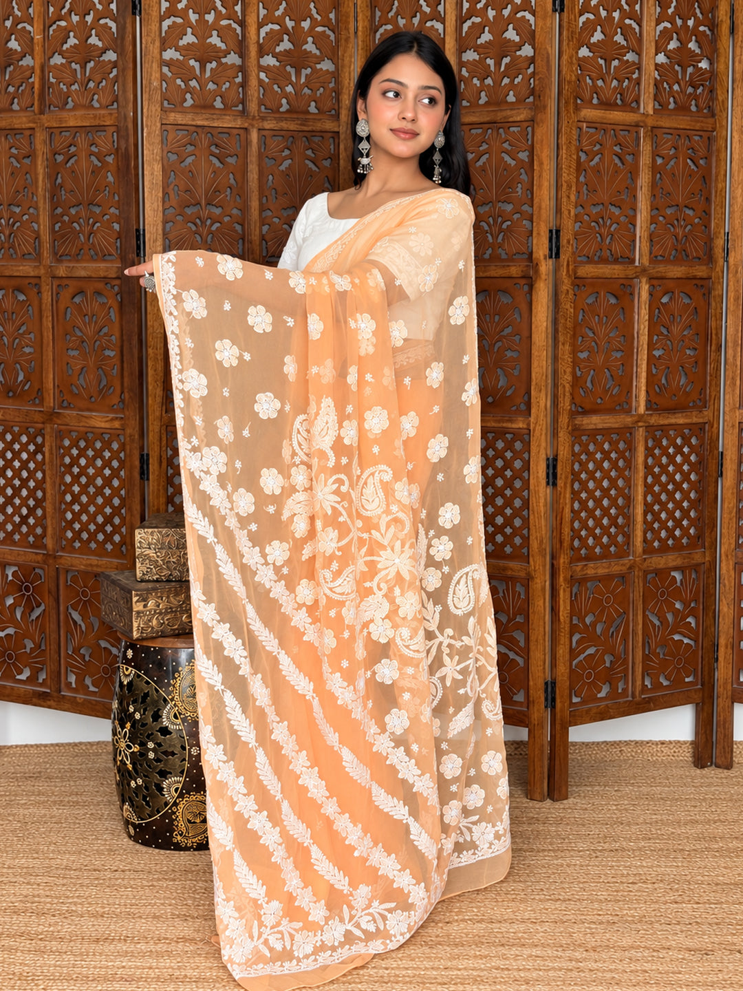 Model wearing the Srija Georgette Chikankari Saree and holding its pallu open to display floral embroidery, paisley motifs and decorative borders.