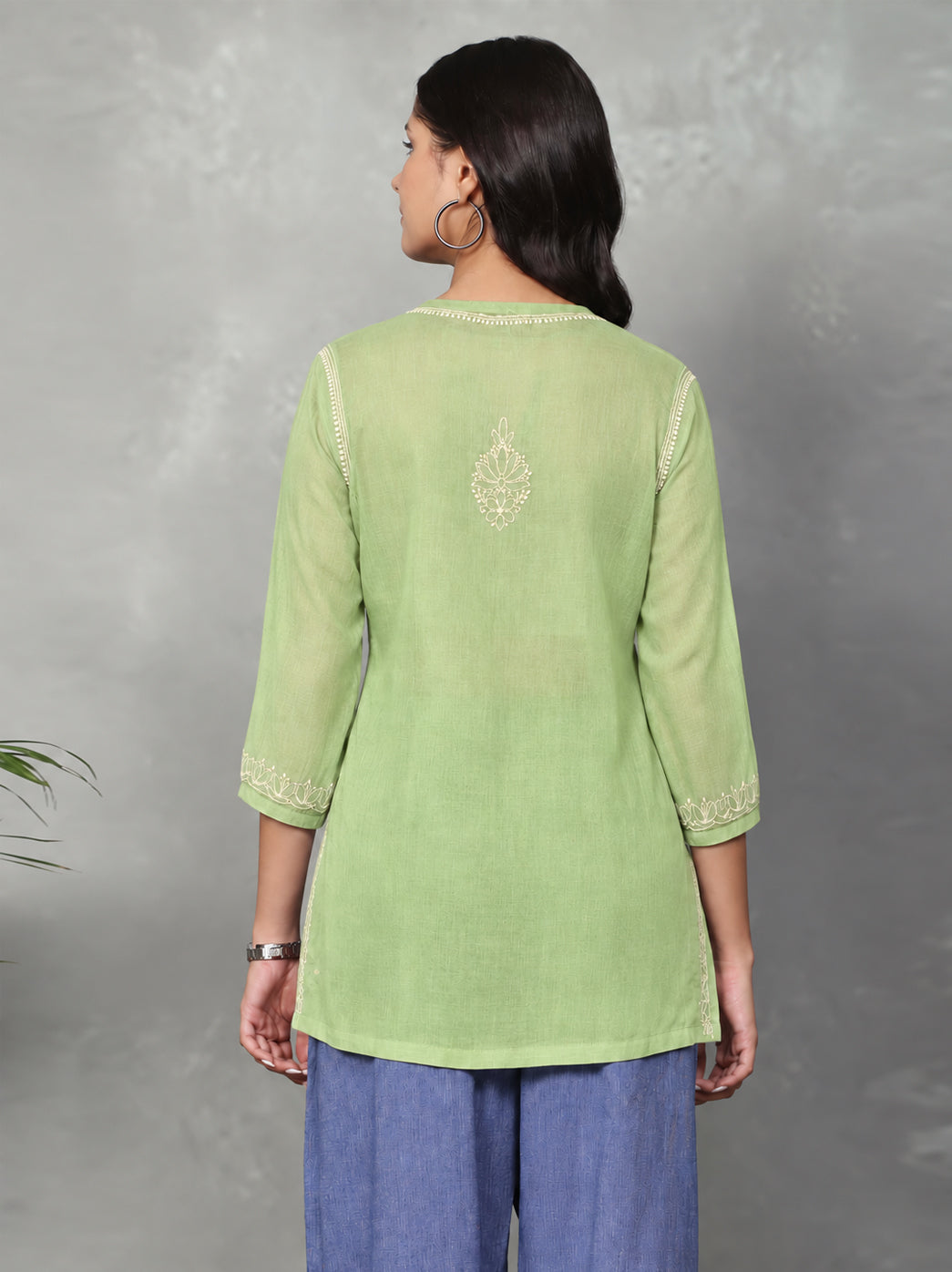 Short Chikankari kurti featuring large botanical motifs interspersed with smaller flowers, complemented by embroidered borders at the sleeve edges and hem.
