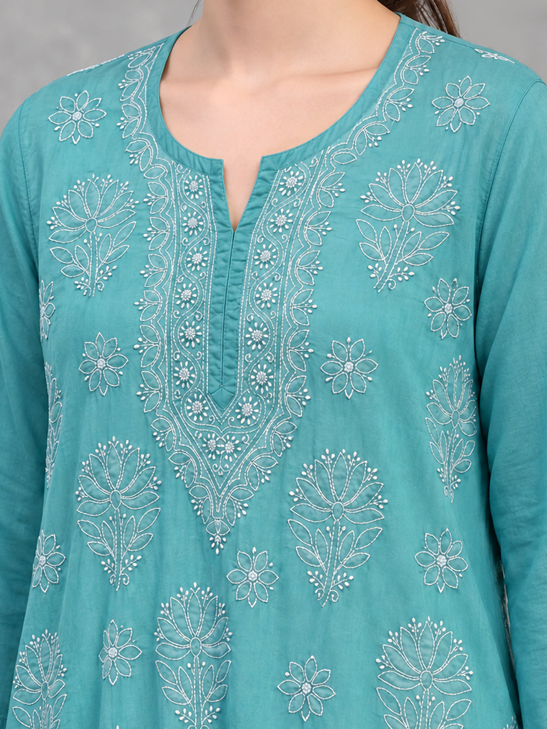 Short Chikankari kurti featuring large botanical motifs interspersed with smaller flowers, complemented by embroidered borders at the sleeve edges and hem.