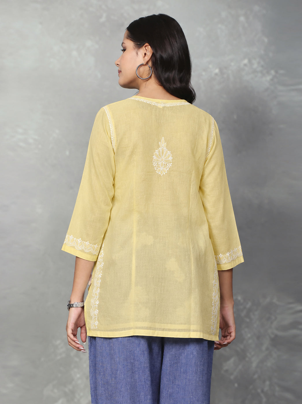 Ziva Cotton Short Kurti by The Chikan Label displayed on a wooden hanger, showcasing its straight silhouette, floral embroidery and three-quarter sleeves.